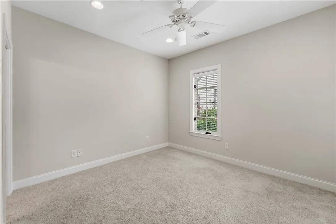 A well-lit bedroom featuring soft carpeting and a window overlooking lush greenery.