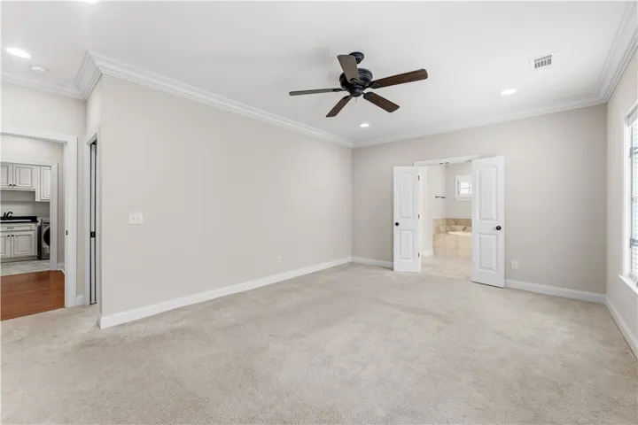 A spacious primary bedroom featuring plush carpet flooring and a sophisticated ceiling fan, leading to an en-suite bathroom.