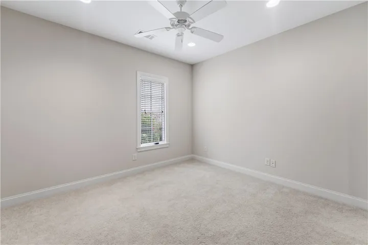 A well-lit bedroom with carpeted floors, a ceiling fan, and a single window offering natural light.
