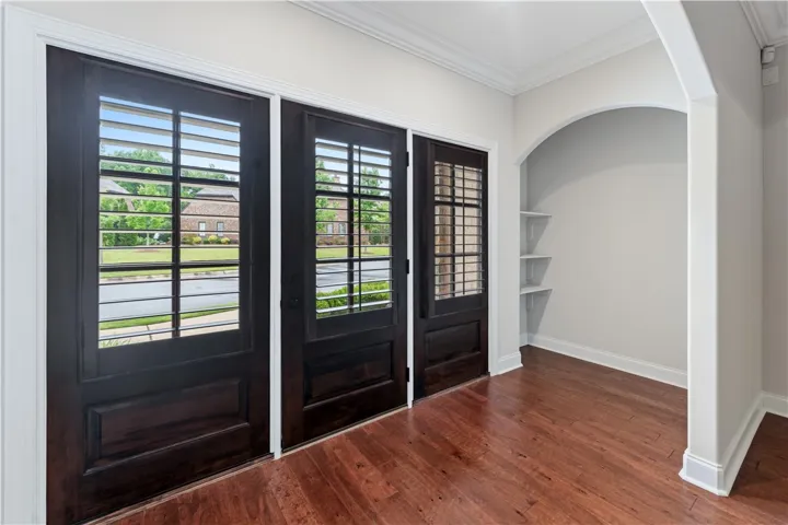 Enter through elegant dark wood doors into a space with gleaming hardwood floors and an arched nook.