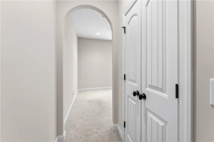 A well-lit interior hallway features an elegant arched entryway and a closed storage closet.
