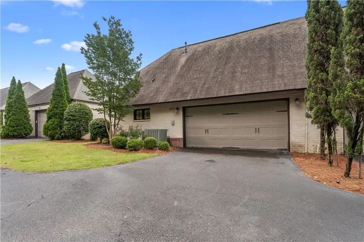A well-maintained paved driveway leads to a double garage set against a backdrop of mature landscaping.