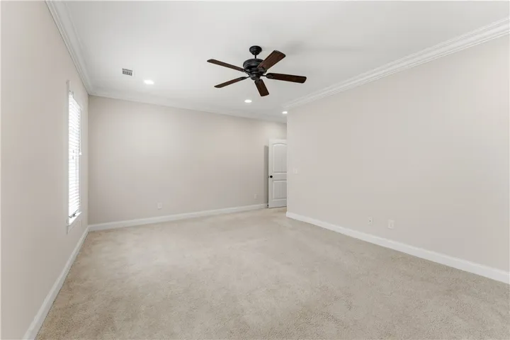 A spacious, naturally illuminated room featuring a ceiling fan and plush carpeting.