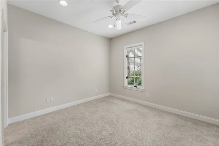 A well-lit bedroom featuring soft carpeting and a window overlooking lush greenery.