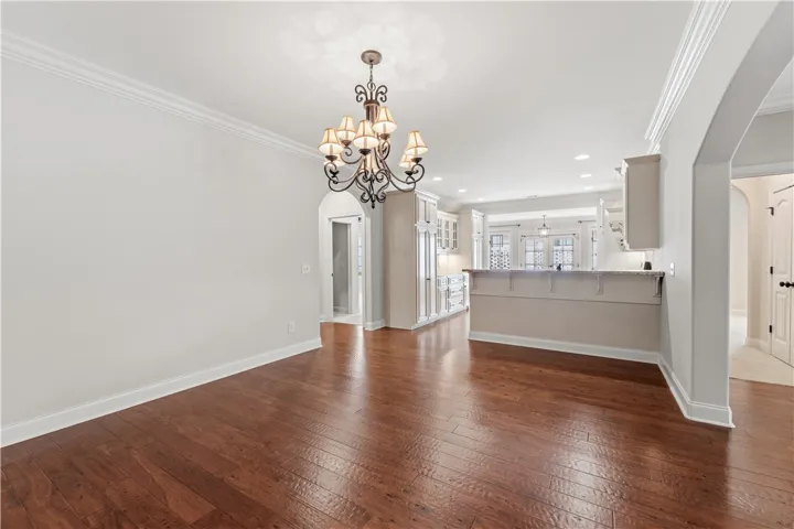 Rich hardwood floors flow through this welcoming dining area, illuminated by a classic chandelier and opening to a well-appointed kitchen.