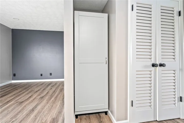 Laminate flooring connects two spaces, one featuring a built-in storage cabinet and a louvered closet.
