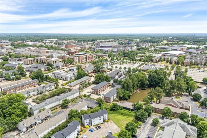 An aerial panorama reveals a dynamic community with dense green landscaping, a tranquil pond, and urban architecture.