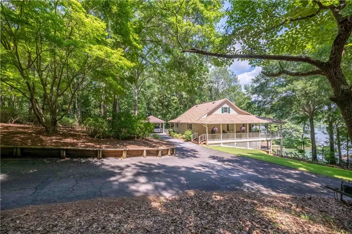 A tranquil lakeside retreat features a sprawling front porch, surrounded by mature trees and a private driveway.