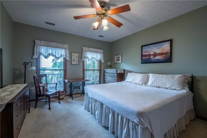 Comfortable bedroom with ample natural light, featuring plush carpeting and a classic ceiling fan.