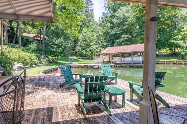 A tranquil lakefront setting featuring a wooden deck and boat house, surrounded by lush trees.