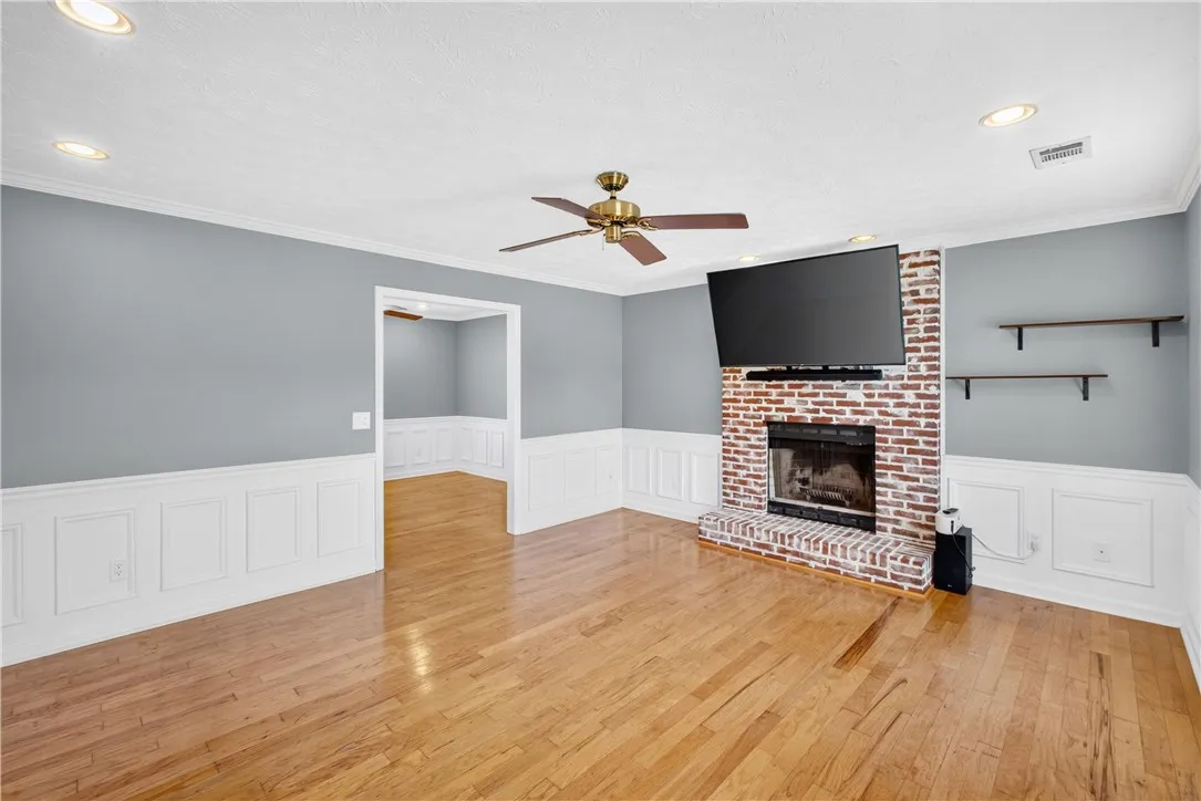 A classic brick fireplace anchors this spacious living area with warm wood flooring and wainscoting.