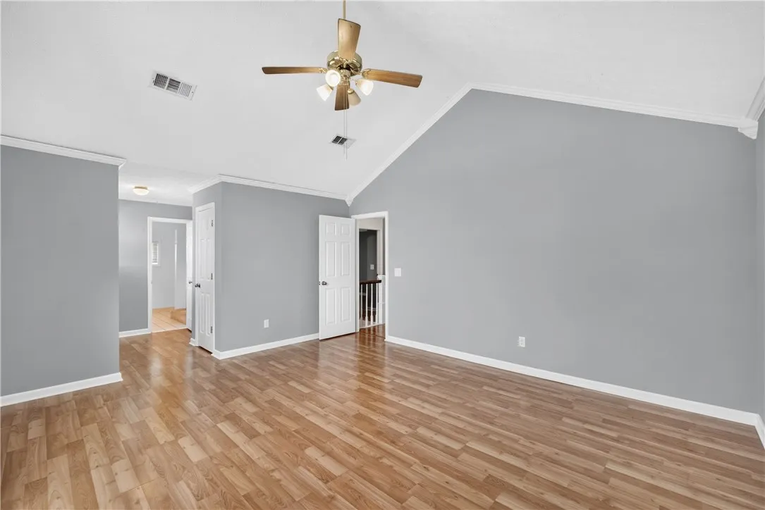 A spacious room features vaulted ceilings, light wood flooring, and a ceiling fan for comfort.
