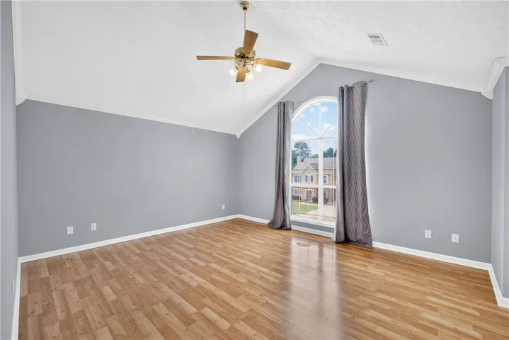 A well-lit room showcasing a vaulted ceiling with a decorative fan and polished wood-look flooring.
