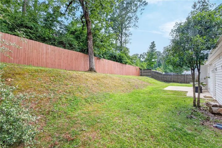 A spacious, sloped yard features mature trees and privacy fencing, ideal for outdoor leisure.