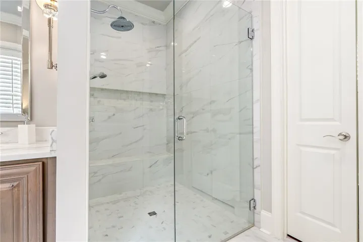 The primary shower features a curbless design, frameless glass, floor-to-ceiling tile, dual shower heads, and generous built-in niche, creating a luxurious bathing experience.