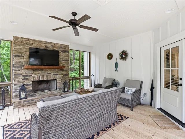 An inviting screened porch features a stone fireplace, ceiling fan, and ample space for relaxation.