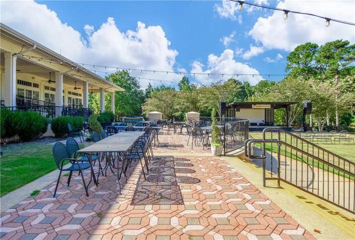 An inviting outdoor patio features ample seating with string lights overhead, adjacent to a stage for entertainment.