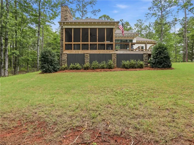 A spacious yard with verdant lawns leads to a screened-in porch and open deck, ideal for outdoor living.