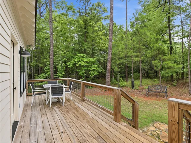 A spacious wooden deck provides ample room for outdoor dining and relaxation amidst a verdant tree-filled landscape.