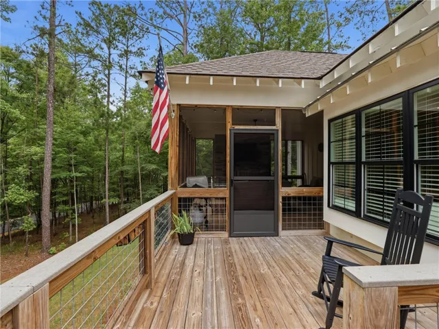 A spacious wooden deck provides ample outdoor living space, complementing the screened porch overlooking verdant forest.