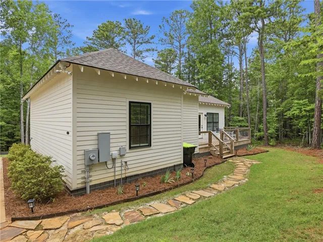 A charming cottage-style residence nestled among mature trees, featuring a cozy outdoor deck.