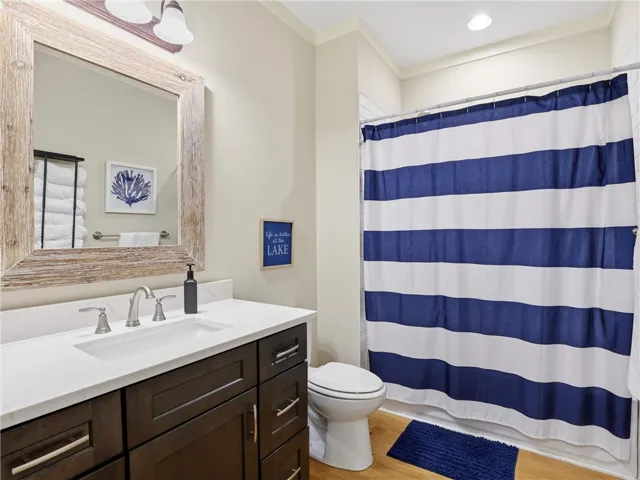 A well-lit bathroom features a rich wood vanity, white countertop, and a shower with a vibrant striped curtain.