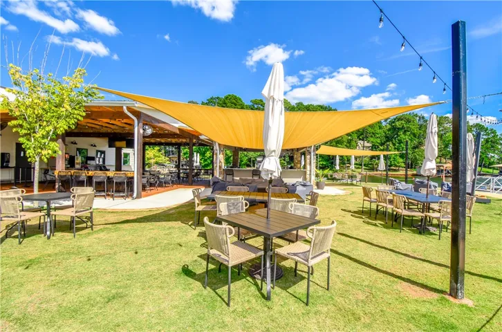 Lush green grass and sail shades create a welcoming outdoor dining and entertainment space with lake views.