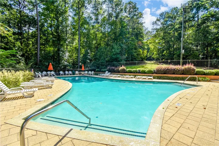 An inviting community pool with ample lounge seating awaits, surrounded by lush green foliage.