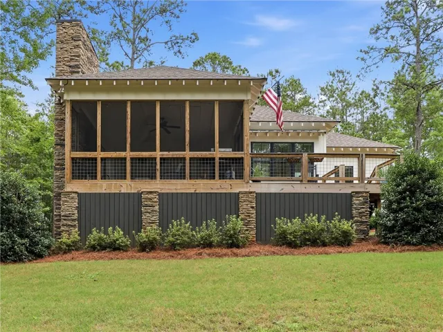 A spacious elevated deck with screened porch and stone pillars overlooks a lush, green yard.
