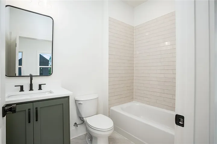 A sleek vanity with a dark green cabinet and modern fixtures complements the tiled shower and bath.