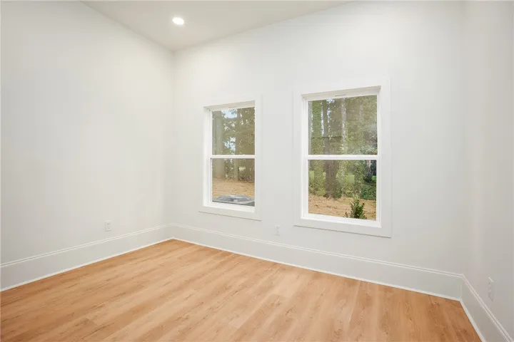 A well-lit room features light wood flooring and windows overlooking a wooded landscape.