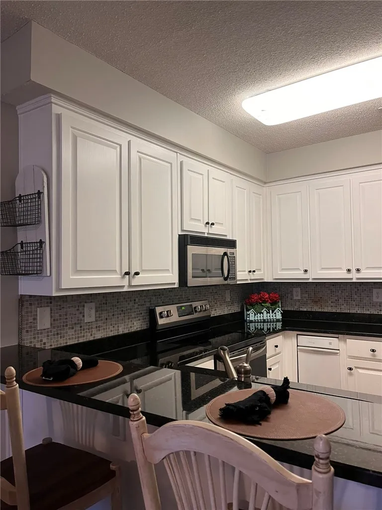 A well-lit kitchen features pristine white cabinetry and dark granite countertops, offering a comfortable breakfast bar.