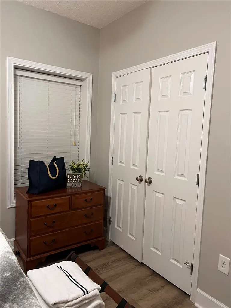 Well-lit room featuring hardwood-style flooring, a double-door closet, and a bright window with blinds.