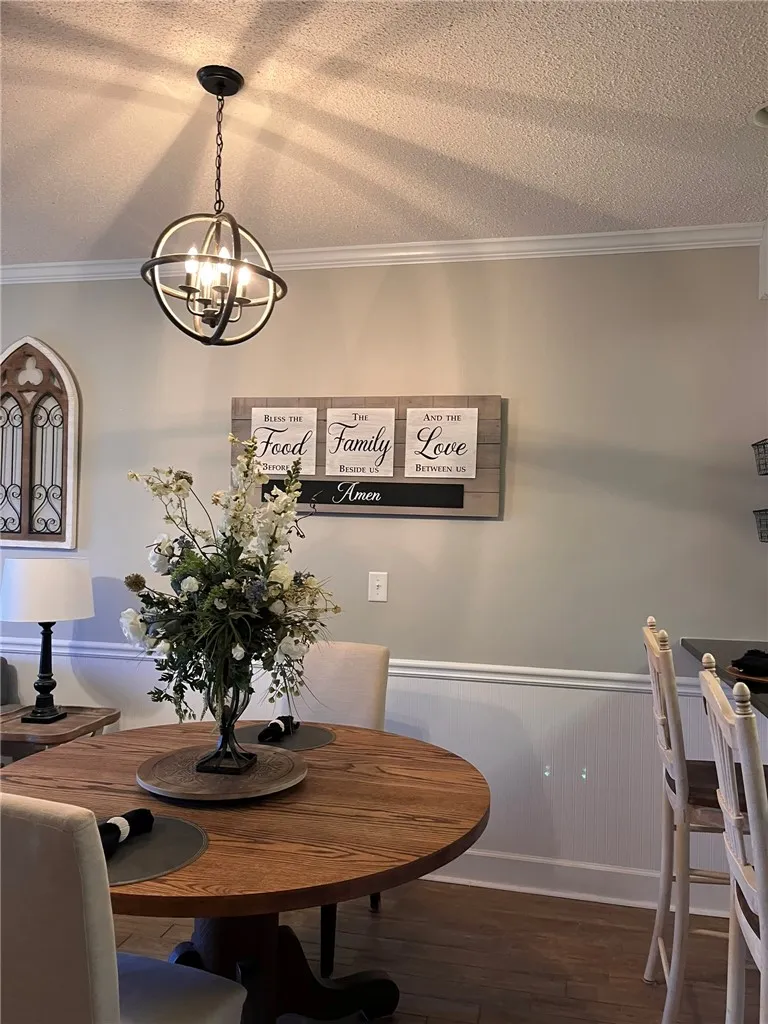 A refined dining area is illuminated by an elegant orb chandelier, featuring rich hardwood flooring.