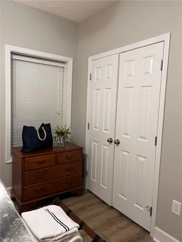 Well-lit room featuring hardwood-style flooring, a double-door closet, and a bright window with blinds.