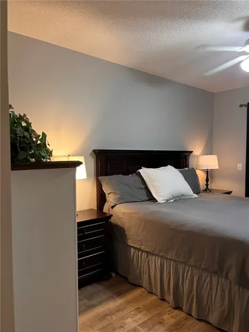 Natural wood-look flooring grounds this restful bedroom, featuring an elegant dark wood headboard and vaulted ceilings.