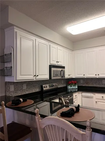 A well-lit kitchen features pristine white cabinetry and dark granite countertops, offering a comfortable breakfast bar.