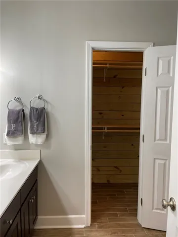 Functional bathroom vanity with a smooth countertop and a spacious walk-in closet featuring warm wooden paneling.
