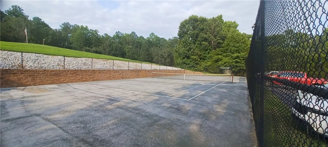 A well-maintained tennis court awaits, bordered by a fence and verdant landscaping.