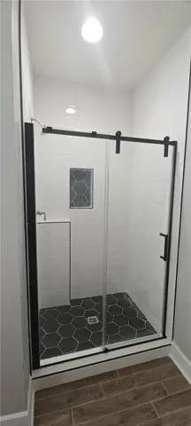 A well-lit shower features sleek glass doors and distinct black hexagonal tile flooring.
