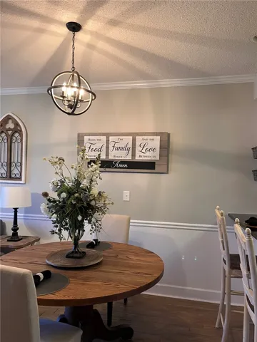 A refined dining area is illuminated by an elegant orb chandelier, featuring rich hardwood flooring.