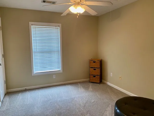A well-lit bedroom features plush carpeting and a modern ceiling fan for ultimate comfort.