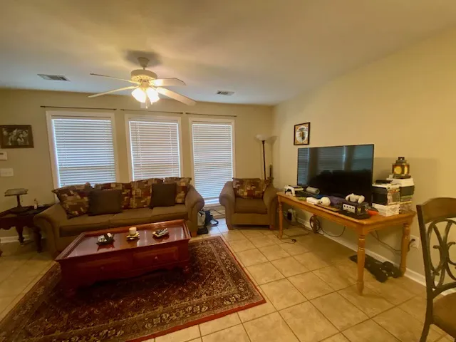 A relaxed living area boasts a ceiling fan, abundant natural light, and durable tile flooring.