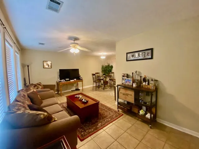 A tiled living room transitions smoothly into a dining area, offering a cohesive and comfortable layout.