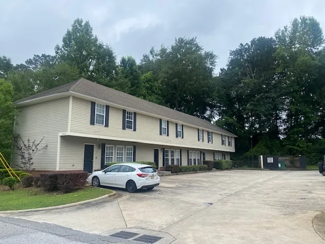 A classic two-story multifamily residence with ample outdoor parking, nestled among mature trees.