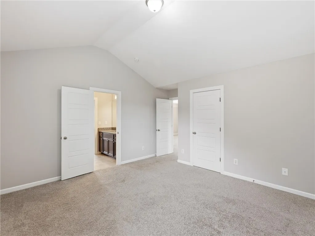 A spacious primary bedroom features soft carpeting, lofty vaulted ceilings, and a private ensuite entry.