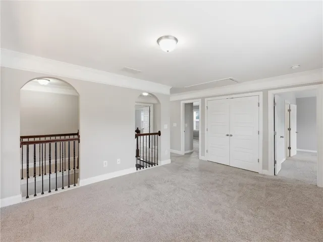 A spacious upper-level bonus room awaits your personalization, featuring plush carpet and elegant arched doorways.