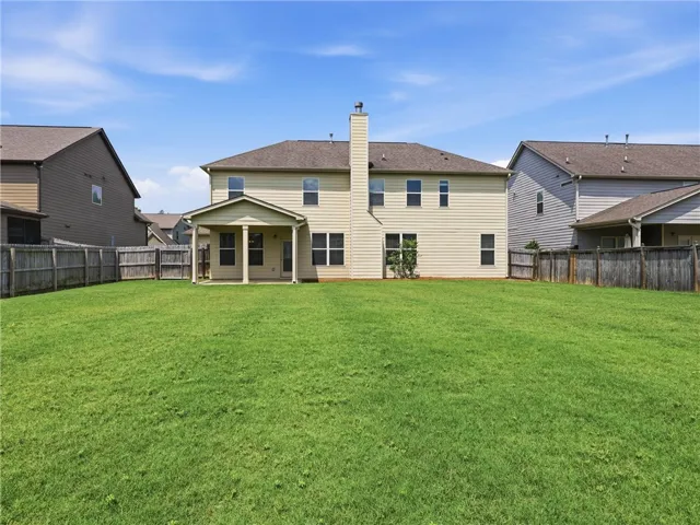 A spacious backyard with vibrant green grass, featuring a covered patio for outdoor relaxation.