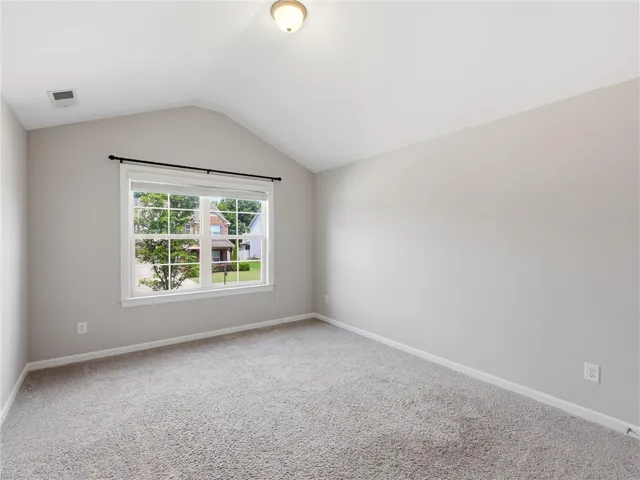 A well-lit bedroom features vaulted ceilings and plush carpeting.