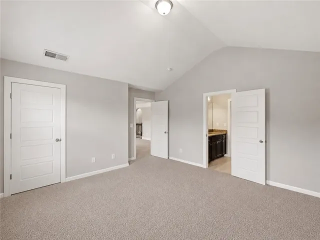 A spacious room offers plush carpeting, a vaulted ceiling, and convenient access to an en-suite bath.